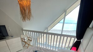 Un dormitorio moderno con una cama grande, una mesita de noche con una lámpara roja y vistas al mar desde un balcón.