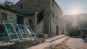 A stone building with a staircase leading to a porch, a small adjacent structure, and a row of green folding chairs in front. - Villa Santarsa, 31 people, magnificent views and private pool, no neighbors (Sansepolcro)