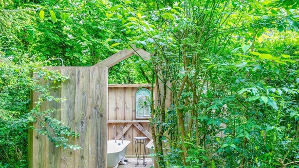 A wooden structure with a bathtub and a small table, surrounded by dense greenery. - Lovely Devon barn, near Exeter, set in 15 acres of countryside (Crediton)