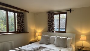 A neatly made bed with white linens and a folded towel, two bedside lamps, and a window with curtains. - Lovely Devon barn, near Exeter, set in 15 acres of countryside (Crediton)