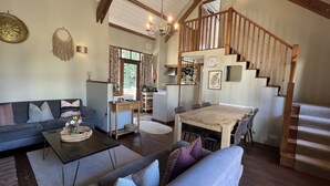 A spacious living area with a sofa, coffee table, and dining table. A staircase leads to an upper level. - Lovely Devon barn, near Exeter, set in 15 acres of countryside (Crediton)