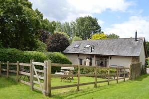 Une maison de campagne au toit en pente, avec une clôture en bois et un banc dans la cour.