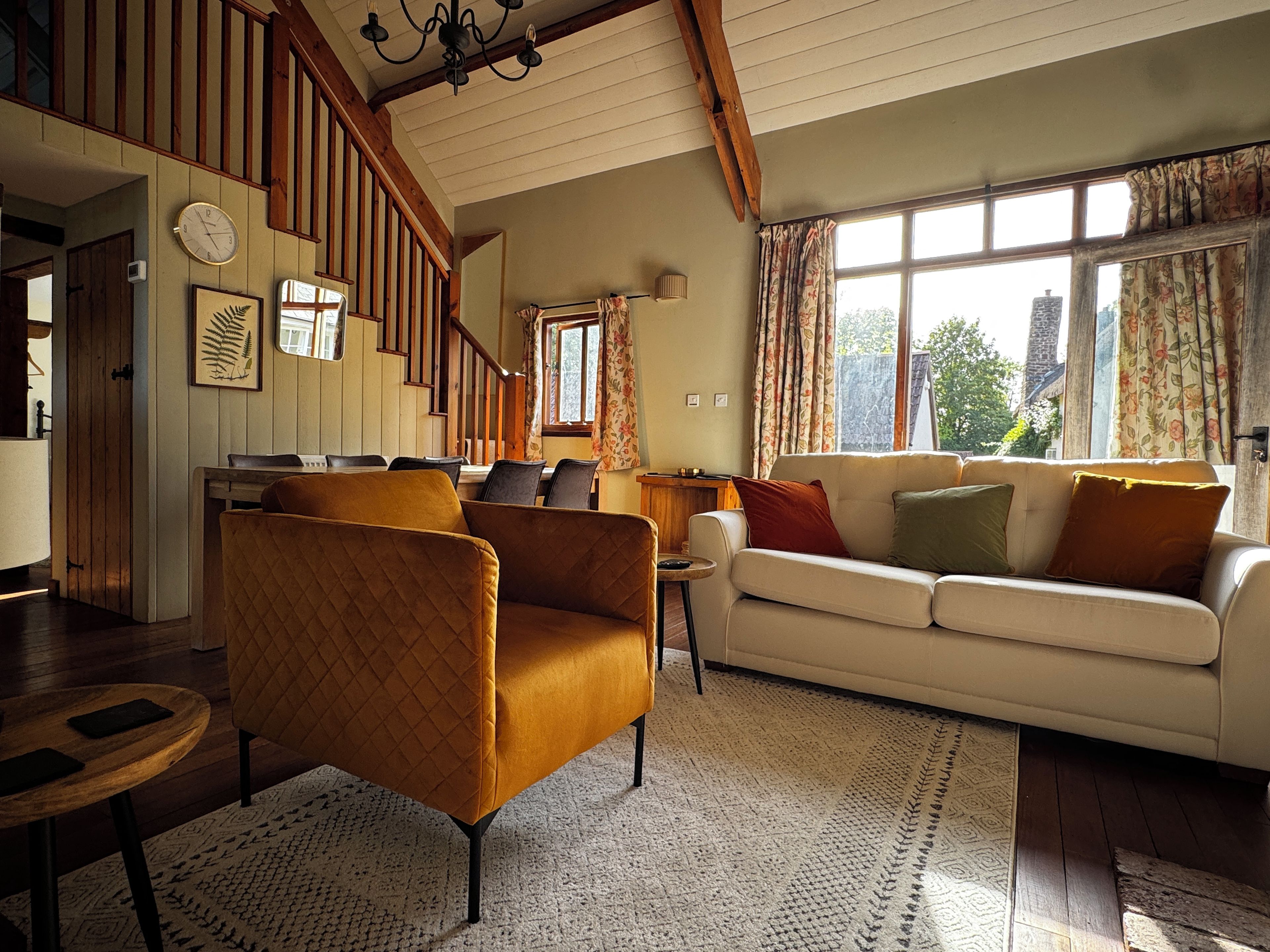 A spacious living room with a staircase, a white sofa, and a brown armchair.
