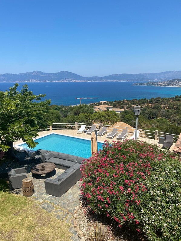 A pool area with lounge chairs and a view of the sea.