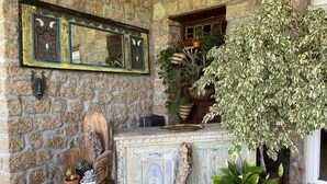 A stone wall with a mirror, a rustic wooden chair, and a variety of potted plants.