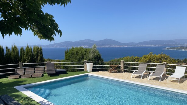 A swimming pool with lounge chairs and a view of the sea and mountains.