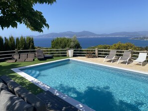 A swimming pool with lounge chairs and a view of the sea and mountains.