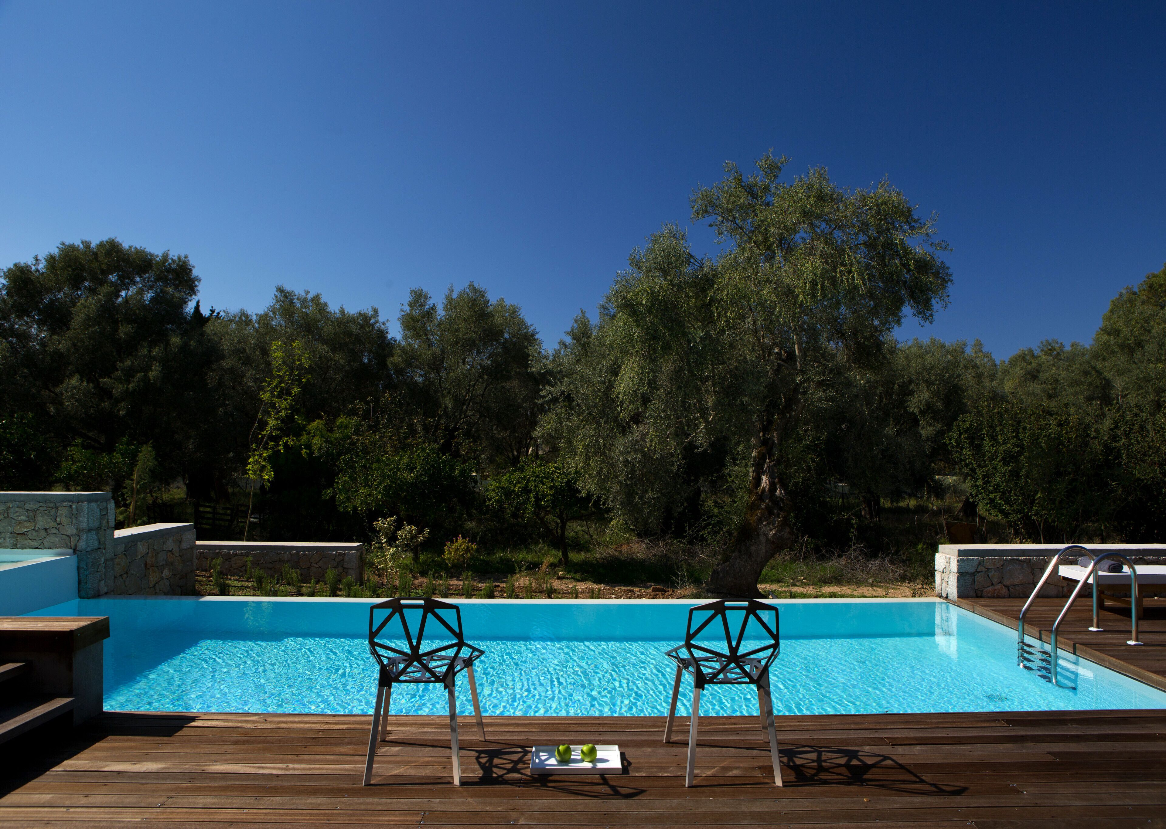 A swimming pool with two chairs facing the water, surrounded by trees and a stone wall.