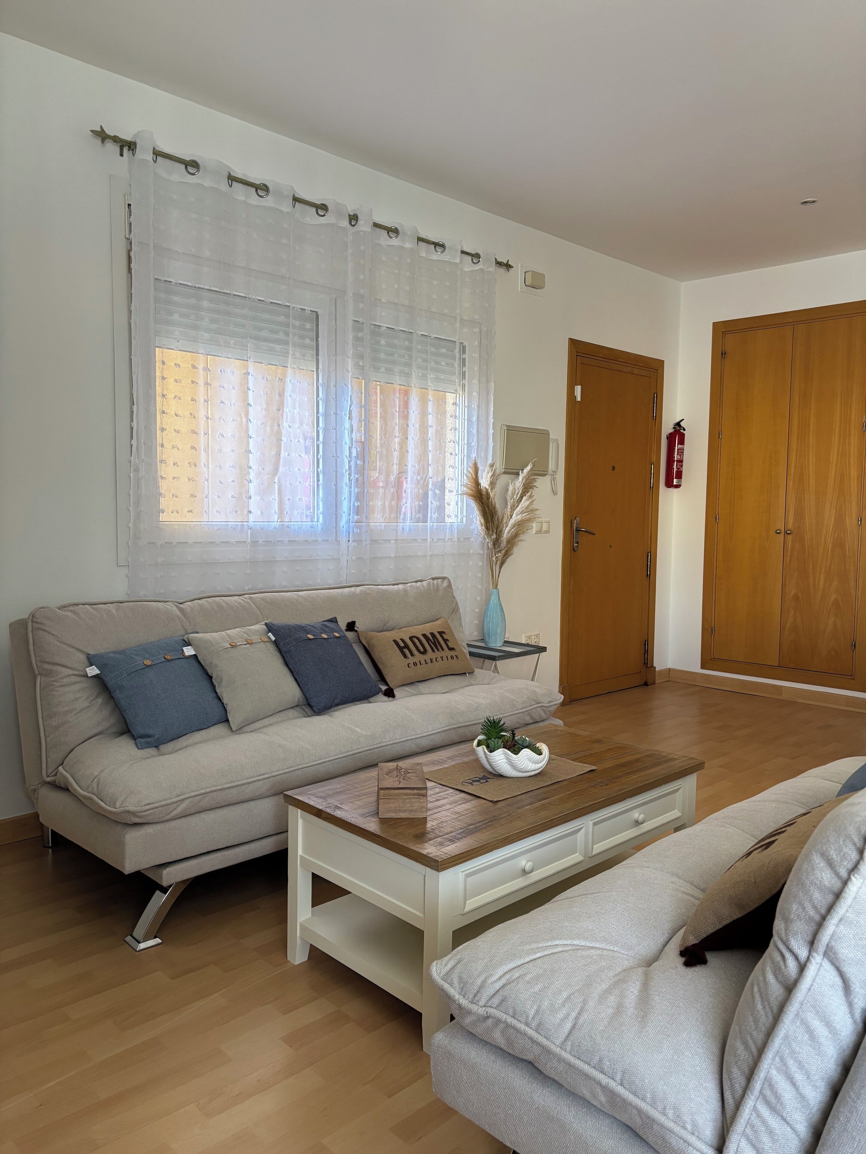 Una sala de estar con un sofá color beige, una mesa de centro de madera y un sillón blanco.