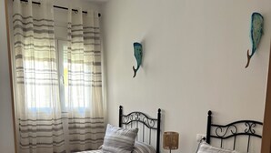 Una habitación con dos camas, cada una con ropa de cama y almohadas a rayas, una mesita de noche con lámpara y una decoración en la pared.