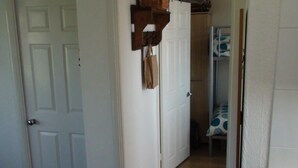 Een gang met een witte deur, een houten plank met een mand, en een gestreept stoel.