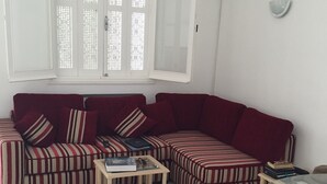 Una sala de estar con un sofá a rayas rojas, una pequeña mesa de centro de madera y una mesa de vidrio con vasos encima.