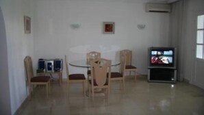 Un comedor con una mesa redonda y cuatro sillas, un televisor sobre un mueble bajo, y cuadros en la pared.
