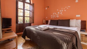A bedroom with a large bed, a television on a wooden stand, and a window with curtains.