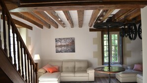 A living room with a wooden ceiling, a beige sectional sofa, a small round table, and a window with blinds.