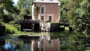 A historic building with a stone facade, a tiled roof, and a small bridge over a calm water body with lily pads.