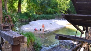 A wooden deck overlooking a small pond with a water wheel and a sandy area.