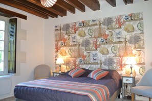 A bedroom with a bed, two bedside tables with lamps, a chair, and a wall with a nature-themed mural.