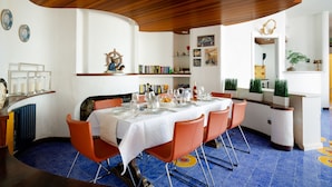 A dining area with a round table set for six, orange chairs, and a blue-tiled floor.