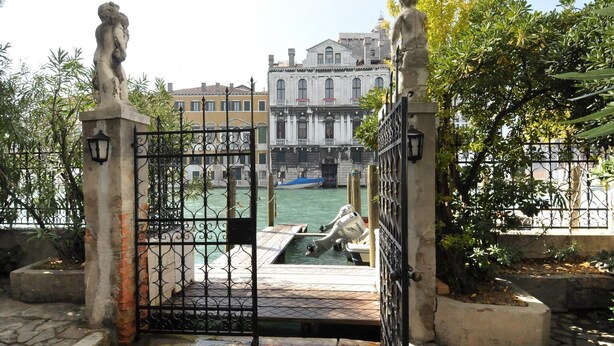 A canal with a boat dock, a stone statue, and a building in the background. - Lovely and quite apartment with garden in the heart of Venice (Venice)