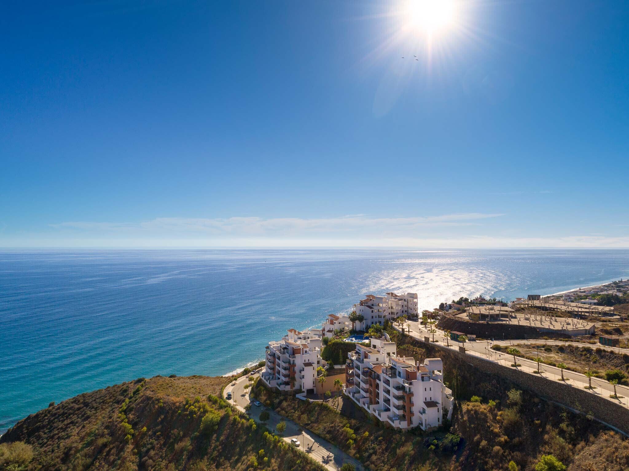 A coastal residential area with buildings overlooking the sea, a clear sky, and a sunny day.