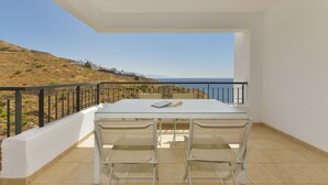 A balcony with a table and chairs, overlooking a coastal landscape.
