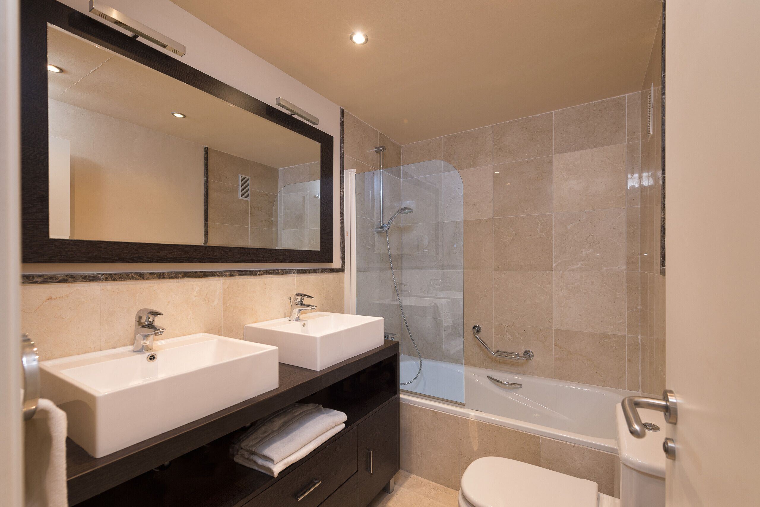 A modern bathroom with two sinks, a large mirror, a shower enclosure, and a bathtub.