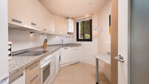A modern kitchen with white cabinets, granite countertops, a built-in oven, a dishwasher, and a window with a view of greenery.