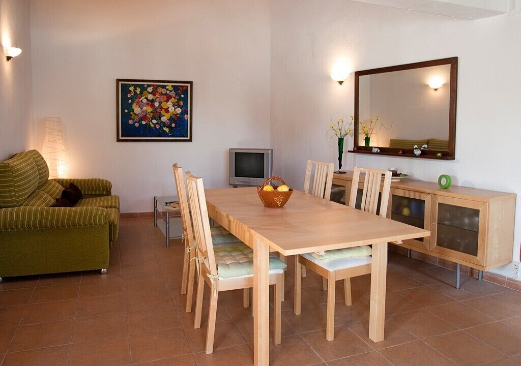 A dining area with a wooden table and chairs, a green sofa, a television, and a painting on the wall.
