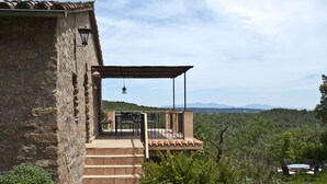 Edifici de pedra amb una escala que condueix a una zona d'estar coberta a l'aire lliure i amb vista al camp.