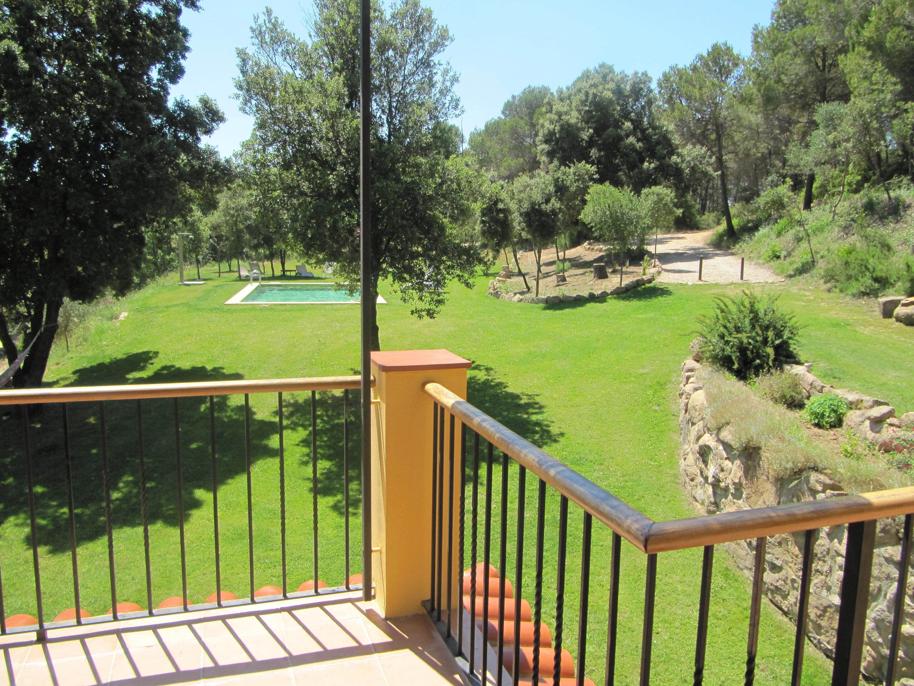 Un balcón con vista a una piscina, zonas verdes y árboles.