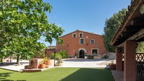 A building with a red facade, a courtyard with artificial grass, and potted plants.