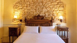 A bedroom with a stone wall arch, a wooden bed, two bedside tables with lamps, and a clock on each table.