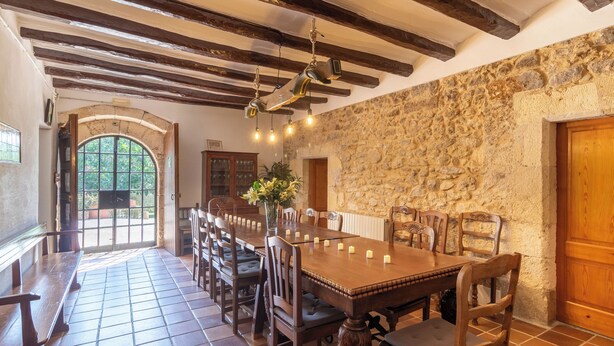 A dining area with a long wooden table, chairs, and a stone wall.