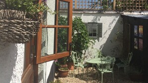 Un pati amb una paret blanca, una porta de fusta, una panxa verda i plantes en testos.