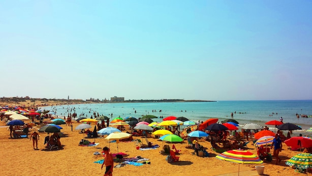 Een druk strand met talloze kleurrijke parasols en mensen die van het water genieten.