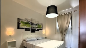 Een slaapkamer met een bed, nachtkastje, een wandlamp, een hangende lamp en een raam met gordijnen.
