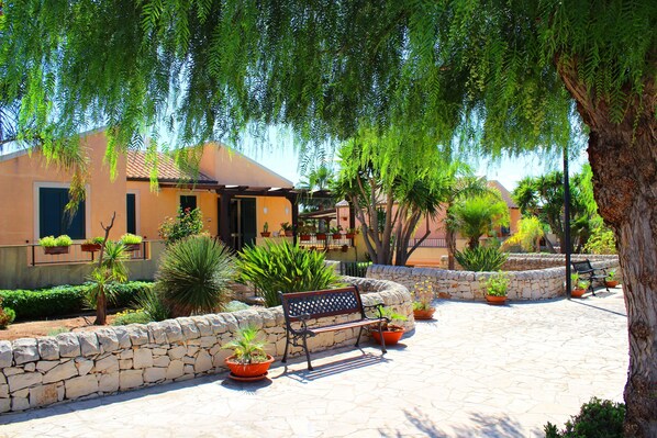 A courtyard with a stone wall, a bench, and potted plants.