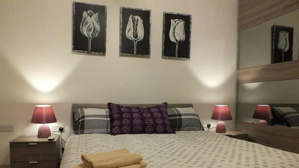 A neatly made bed with a polka dot bedspread, two pillows, a folded towel, and a nightstand with a lamp.