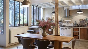 Eine Küche mit Holztisch, Stühlen, einer Vase mit Blumen und einem großen Fenster mit Blick auf Bäume.