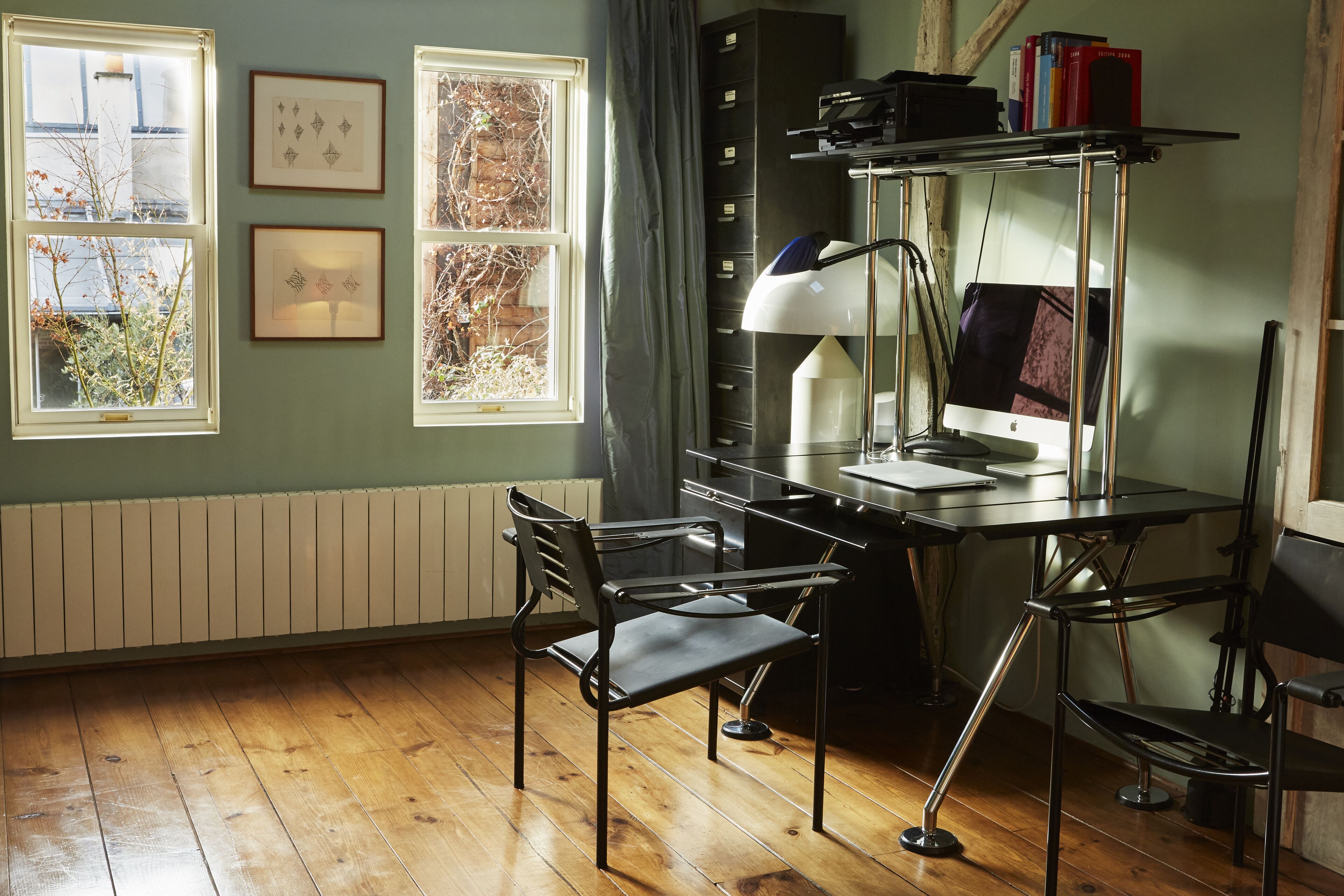 A study room with a desk, two chairs, a computer, and framed pictures on the wall.