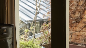 Eine Glastür öffnet sich zu einem Garten mit Topfpflanzen und Blick auf ein Gebäude mit einem Metall-Dach.