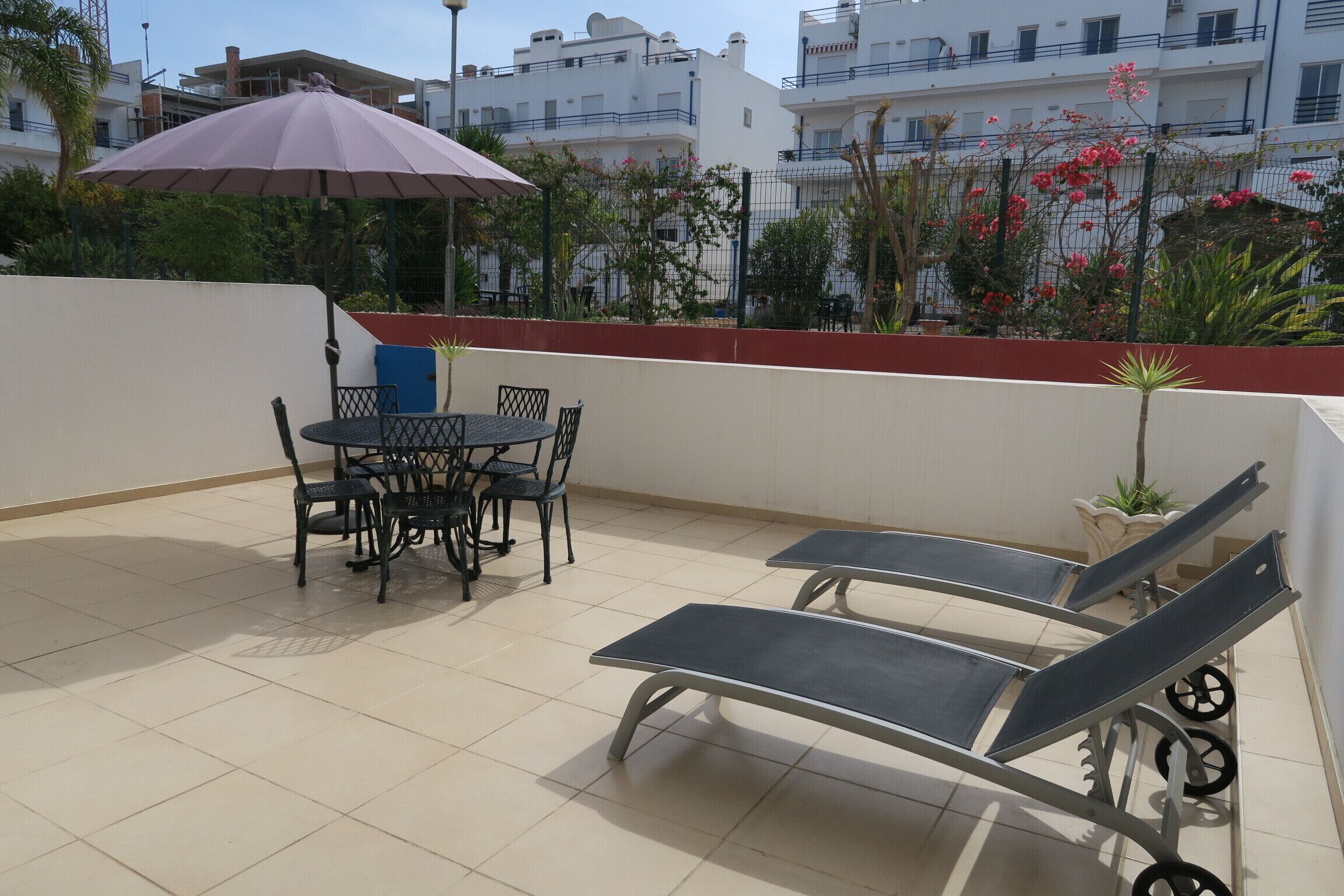 Un patio con una mesa, sillas y una tumbona, además de una sombrilla.