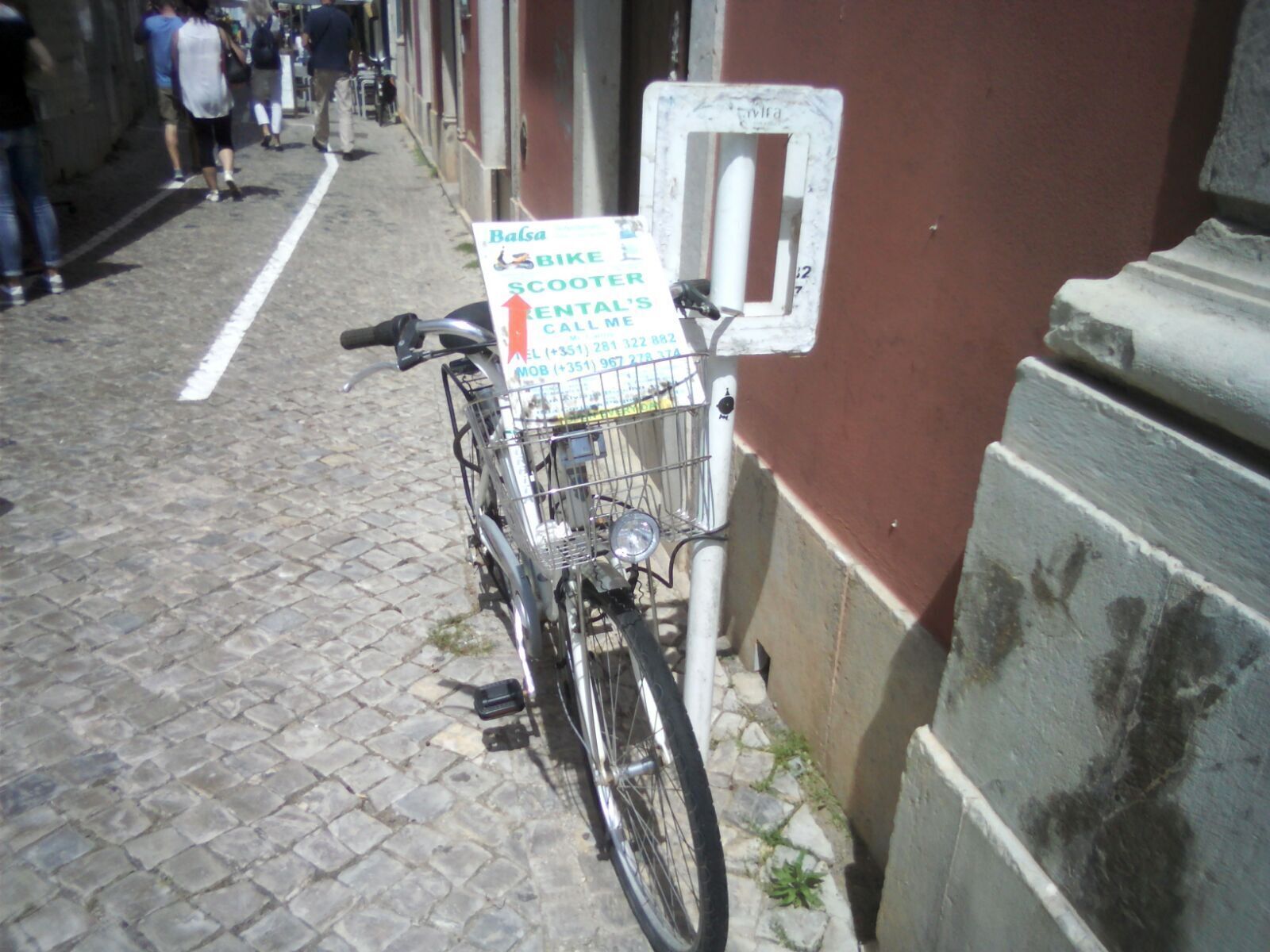 Una bicicleta estacionada en una calle adoquinada con un cartel que anuncia alquiler de bicicletas.