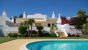 A pool area with a white building in the background, surrounded by greenery and palm trees. - Villa Meia-Praia, with Terrace, Pool and Garden (Lagos)