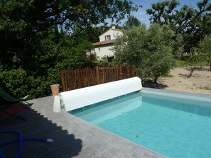 A swimming pool with a wooden deck, surrounded by greenery and a house in the background.