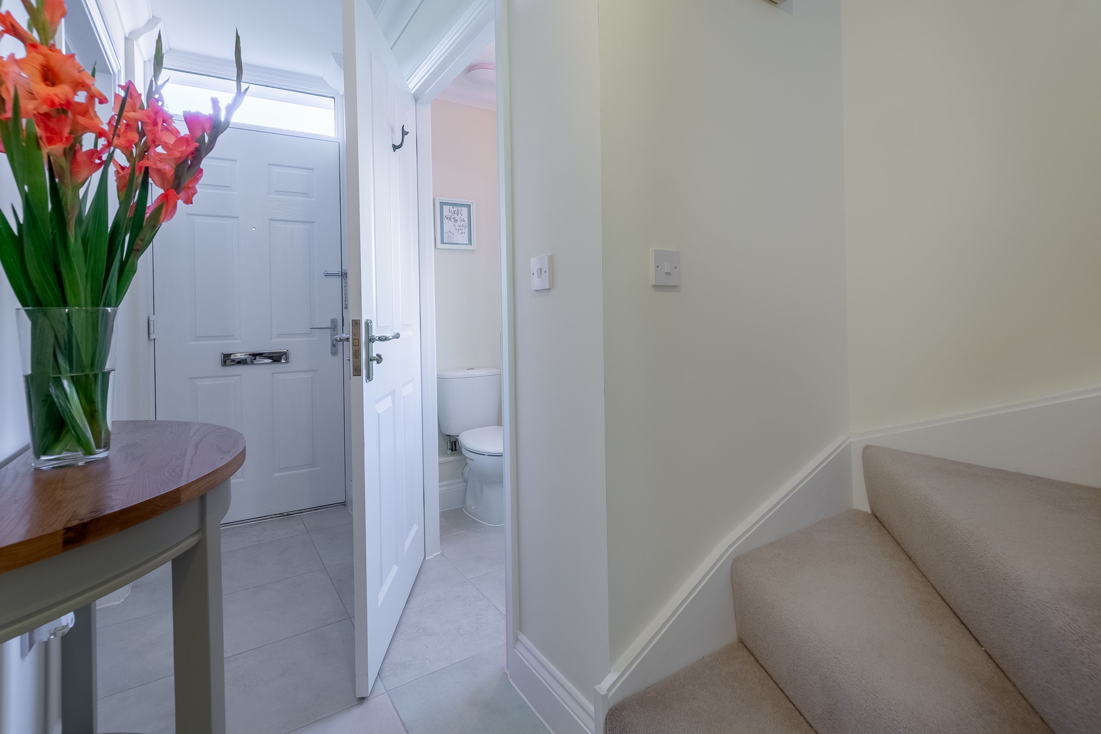 A hallway with a wooden table, a vase with flowers, a white door, and a beige carpeted area.