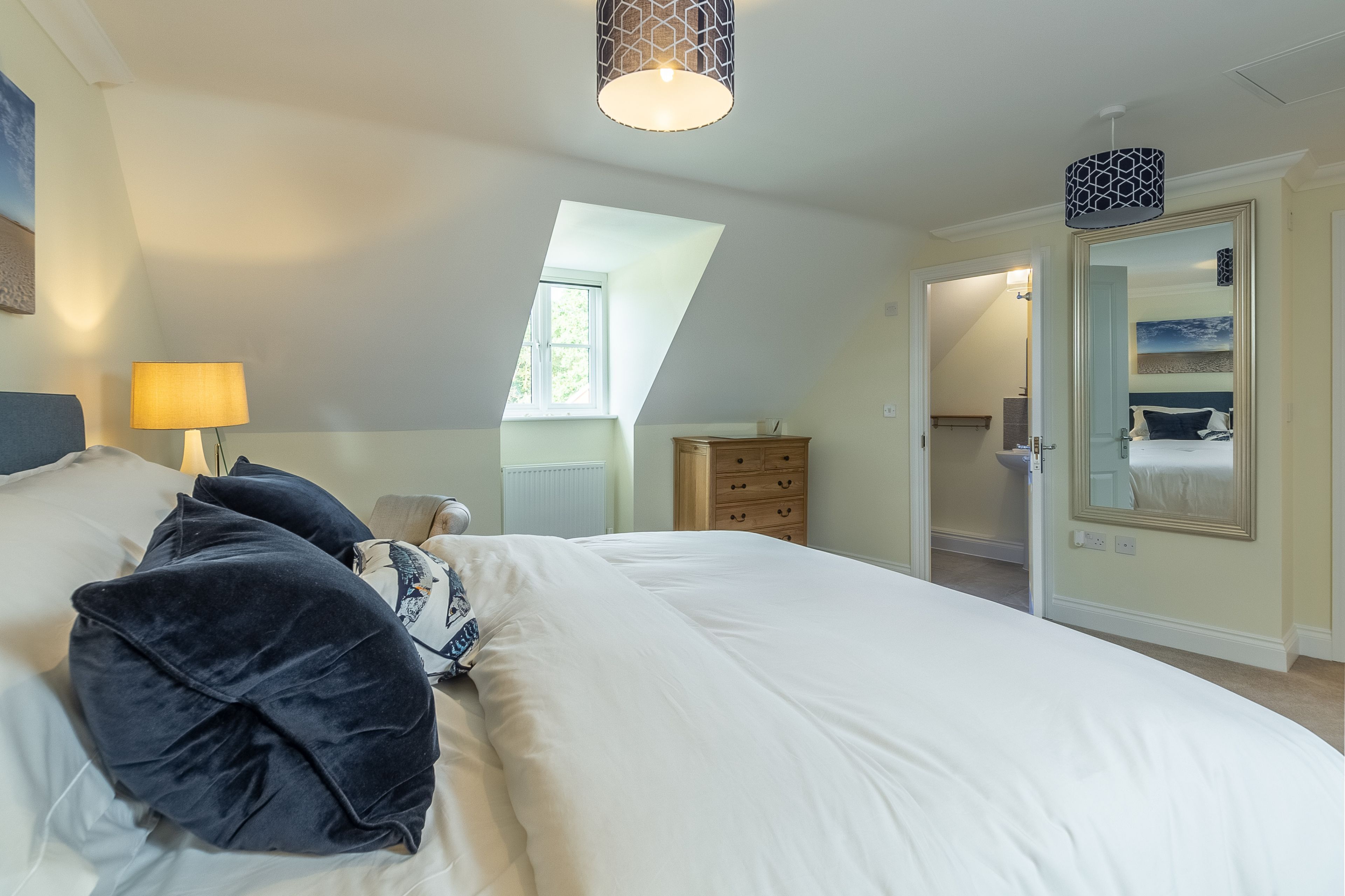 A bedroom with a large bed, a dresser, a mirror, and a skylight.