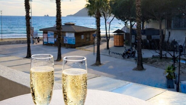 Two champagne glasses on a table with a view of the beach and palm trees.