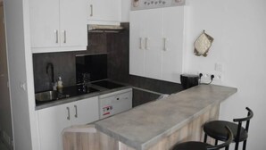 A compact kitchen with white cabinets, a black countertop, and a small island with two chairs.